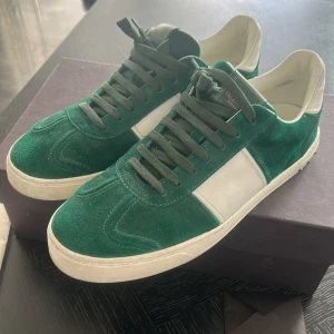Valentino Garavani gröna sneakers mocka - Gröna och vita sneakers från Valentino Garavani i lyxig mocka med vita skinnpaneler. Snygga nitar baktill på sulan och klassisk snörning. Skorna har rund tå och platt sula, perfekt för dig som vill sticka ut med stilrena detaljer.