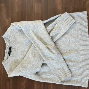 Grå stickad tröja från H&M - En enkel och stilren grå stickad tröja från vero Moda,Tröjan har rund halsringning, långa ärmar och breda ribbade muddar vid ärmslut och nederkant. Perfekt för lager-på-lager och chill dagar.