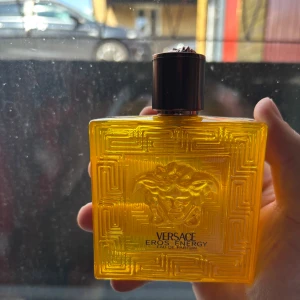 Versace Eros Energy Eau de Parfum - Versace Eros Energy pour homme, Eau de Parfum 100 ml. Flaskan är fyrkantig och genomskinligt gul med Versaces ikoniska Medusa-huvud i relief och geometriskt mönster. Snygg och lyxig design med svart kork och guldig kartong.