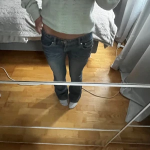 Lågmidjade blå bootcut jeans med krona - Säljer ett par blå jeans med låg midja och bootcut passform. Jeansen har en snygg tvätt och en blingad krona på bakfickan som ger extra edge. Perfekta för dig som gillar 00-talsvibe och vill sticka ut lite extra. 39cm i midje bredd och passar nån som är runt 165-170