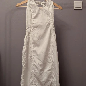 Vit ärmlös långklänning med knyt - Snygg vit långklänning med ärmlös design och knytning i nacken. Klänningen har en enkel och stilren look med fina sömdetaljer längs sidorna. Perfekt för sommarens varma dagar och passar till många olika stilar.