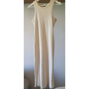 Ribbad långklänning från Kappahl XS - Lång, ribbad klänning från Kappahl i en ljus beige ton. Ärmlös modell med rund halsringning och figurnära passform. Tillverkad i mjuk mix av polyester och bomull, perfekt för en clean och stilren look.