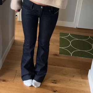 Lågmidjade bootcut jeans från Diesel - Snygga mörkblå jeans från Diesel med bootcut passform och råa, fransiga benslut. Klassisk femficksmodell med dragkedja och detaljerade nitar. Jeansen är i kraftigt denimtyg och har låg midja. Perfekta för en cool och avslappnad stil. Passar någon som är runt 160 