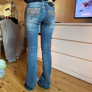 Blå bootcut jeans med broderade fickor - Säljer ett par snygga blå bootcut jeans från Moss me med broderade detaljer på bakfickorna. Jeansen har normal midja och klassisk femficksdesign. Perfekta för dig som vill ha en cool och unik look med extra detaljer baktill💙