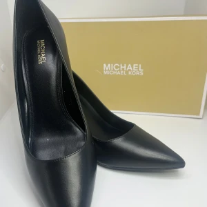 Svarta pumps från Michael Kors - Klassiska svarta pumps från Michael Kors, ”Milly Flex Pump” i äkta skinn. Säljs pga att de är för små, storlek 39 men tajta. De är helt nya och oanvända. Jag säljer de för 1000kr🫶🏽