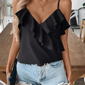 Svart volangtop med smala axelband - Supersnygg svart topp med smala axelband och stora volangdetaljer framtill. Sitter löst och har en feminin v-ringning. Perfekt att styla med jeans eller kjol för en trendig look.