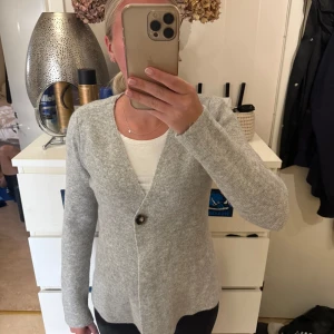 Ljusgrå stickad cardigan jacka - Supermjuk och stilren ljusgrå stickad cardigan jacka med en enkel knapp framtill. Jackan har lång ärm och en clean, rak passform som är lätt att matcha med allt. Perfekt för lager-på-lager och chill vardagsstil.