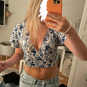 Blommig croppad blus med v-ringning - Superfin croppad blus med blått blommönster. Tröjan knyts fast bak vid ryggen, om intresserad är de bara att fråga om bild!💗