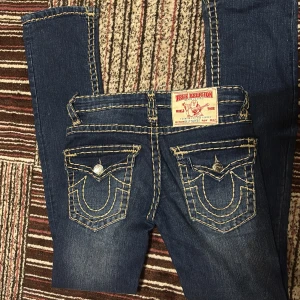 True Religion jeans Billy Super T - Säljer ett par mörkblå True Religion jeans Billy Super T med ikoniska kontrastsömmar och snygga fickdetaljer bak. Tjejen i bilderna är ~172-173 cm och har oftast på sig XS eller XXS. Byxorna är inte så bootcut eller flared 