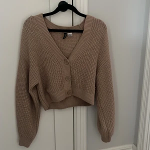 Beige  kofta från H&M Divided - Säljer en beige, kofta från H&M Divided. Tröjan är stickad med grov struktur, har djup v-ringning och stora knappar framtill.
