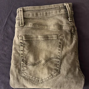 Grå jeans från Jack & Jones - Säljer ett par grå jeans från Jack & Jones med klassisk femficksdesign och raka ben. Jeansen har normal passform och är tillverkade i ett mjukt denimtyg. Perfekta för dig som gillar en enkel och stilren look.