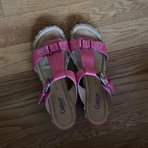 Rosa sandaler med klack från Gabor - Säljer ett par rosa sandaler från Gabor med snygga spänndetaljer och klack. Skorna har en randig plattform i flera färger och öppen tå. Perfekta för dig som vill ha både stil och komfort i sommar.