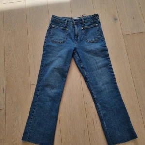 Blå raka jeans från Zara - Säljer ett par klassiska blå jeans från Zara i modell med lite utsvängda , croppade ben och. Jeansen har fem fickor, bälteshällor och stängs med dragkedja och knapp. Perfekta till vardags och lätta att matcha med olika toppar. Aldrig använda