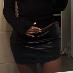 Svart skinnkjol i minilängd - Säljer en svart, tight minikjol i skinnimitation. Kjolen har en slät yta och klassisk passform som sitter högt i midjan. 150 kr 