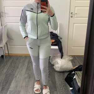 Grå mjukisbyxor från Nike - Säljer ett par grå mjukisbyxor från Nike med svarta detaljer och logga på benet. Byxorna har resår i midjan och smal passform nedtill. Perfekta för en avslappnad stil.