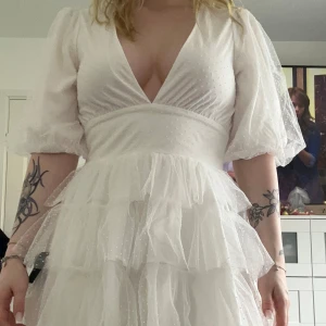 Vit kortklänning med volang - Superfin vit klänning från Lulus med djup v-ringning, puffärmar och flera lager volang i kjolen. Klänningen har en markerad midja. Aldrig använd och lapparna sitter kvar