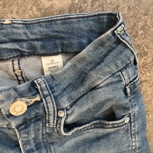 Blå skinny jeans med hög midja - Säljer ett par klassiska blå skinny jeans med hög midja och smal passform. Jeansen har fem fickor, dragkedja och knapp framtill. Perfekta till vardags och lätta att matcha med olika toppar.