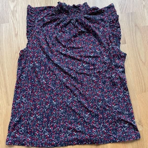 Söt blommig topp från Holly & Whyte - Supersöt blommig topp från Holly & Whyte i marinblått med röda och vita detaljer. Toppen är ärmlös, har resår upptill och är gjord i mjuk bomull. Perfekt för varma dagar när du vill känna dig både bekväm och fin 🌸
