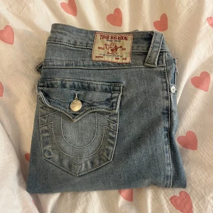 True Religion Joey Low Rise Flare Jeans - Säljer ett par klassiska blå jeans från True Religion, modell Joey med låg midja och utsvängda ben. Snygga detaljer på bakfickan och silverfärgade knappar. Perfekta för dig som gillar en retro vibe och vill sticka ut lite extra. Fint skick säljs då de är för små! Strl 28 