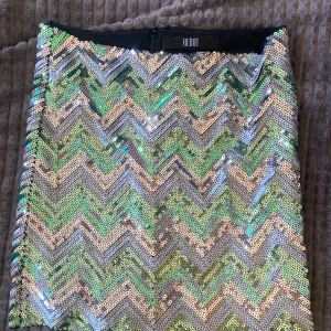Paljettkjol med zickzackmönster från Bedo - Säljer en glittrig kjol från Bedo med paljetter i zickzackmönster i grönt, silver och beige. Kjolen är kort och perfekt för dig som vill sticka ut. Dragkedja bak för enkel på- och avtagning.