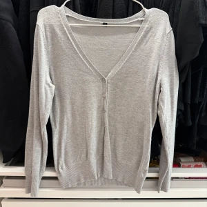 Ljusgrå v-ringad kofta - Säljer en ljusgrå v-ringad kofta med knappar framtill. Tröjan har lång ärm och är tillverkad i ett mjukt, tunt stickat material. Perfekt att slänga över en topp eller klänning.