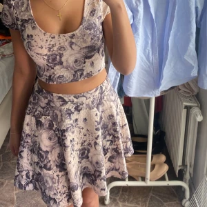 Blommig kjol med matchande topp - Tvådelad klänning med blommigt mönster. Kjolen är kort och utsvängd, toppen är croppad med rund halsringning och korta ärmar. 