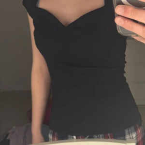 Svart omlottopp med v-ringning - Säljer en svart topp med omlottdesign och v-ringning. Toppen har korta ärmar och sitter tight. Perfekt för dig som vill ha en stilren och enkel look.