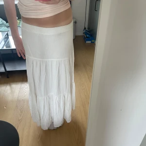Vit långkjol från Stradivarius - Säljer en vit långkjol från Stradivarius med volangdetaljer. Kjolen har en luftig och flowy passform, perfekt för varma dagar. Tillverkad i ett lätt material som ger en avslappnad och somrig känsla. Säljer då den inte kommer till användning🌸