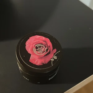 British Rose Exfoliating Gel Body Scrub - En exfolierande gel body scrub från The Body Shop i doften British Rose. Kommer i en svart burk med ros-motiv på locket och innehåller 50 ml. Gelen har en rosabrun färg och är perfekt för att ge huden en fräsch känsla.