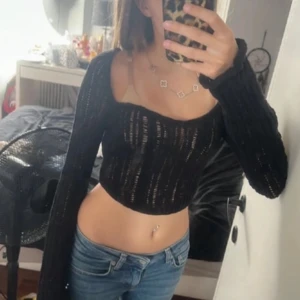 Svart croppad stickad topp med snörning - Trendig svart croppad topp i stickat material med långa ärmar och snygg snörning i ryggen. Fyrkantig urringning och genombrutet mönster ger en cool look. Perfekt för att lyfta din outfit.
