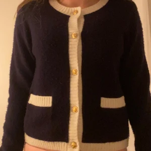 Mörkblå kofta med vita detaljer från RYVLS - Säljer en mörkblå kofta från RYVLS med vita ribbade kanter och guldknappar. Koftan har två fickor framtill och är långärmad. Perfekt för lager-på-lager och enkel att matcha med olika outfits. 💕 