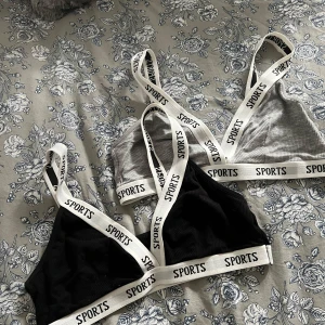 2-pack sporttoppar  - Två sportiga ribbade toppar i svart och grått med breda axelband och resår med texten 'SPORTS'. Perfekta för träning eller som bekväma vardagstoppar. Säljs som ett set.