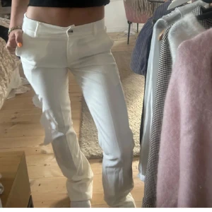 Vita kostymbyxor från Chelsea - Säljer ett par vita kostymbyxor från Chelsea med klassisk passform och raka ben. Byxorna har normal midja, knapp och dragkedja framtill samt bälteshällor. Perfekta för en stilren look.