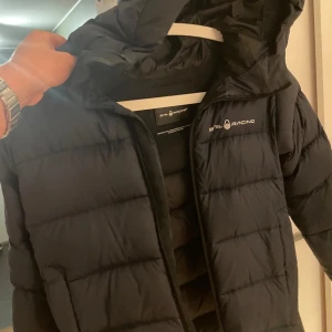 Svart dunjacka från Sail Racing - Säljer en mörkblå dunjacka från Sail Racing i mycket bra skick. Jackan är perfekt för vintern med sin quiltade design och långa ärmar. Den har en praktisk dragkedja och en skön huva för extra värme. Perfekt för kalla dagar! ❄️Det är storlek 150 men den är väldigt stor i storlek och passar dig som är runt 160 cm lång. Den är som ny annars inprisip och dig varm under vintern utan problem! Den är köpt på sailring föra vintern för 3300kr och jag säljer för, 999 skriv vid intresse och frågor!🤩✌️