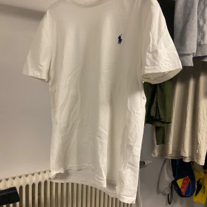 Vit t-shirt från Ralph Lauren - Klassisk vit t-shirt från Ralph Lauren med liten blå broderad logga på bröstet. T-shirten har rund hals och korta ärmar, perfekt för en enkel och stilren look . Nästan aldrig använd, nypris 1099, lite skrynklig eftersom den legat vikt länge. Sitter som en xs-s