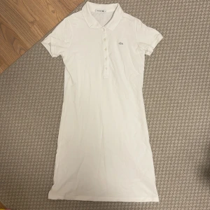 Vit klänning från Lacoste - Säljer en klassisk vit klänning från Lacoste med krage och knappslå framtill, storleken är 38 oanvänd