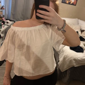 Vit offshoulder blus - Säljer en söt vit offshoulder blus med korta, vida ärmar. Blusen har en lätt rynkad struktur och är perfekt för varma dagar. Enkel och stilren design som passar till mycket.