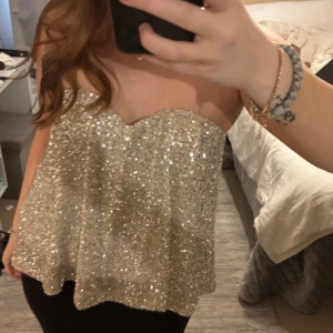 Glittrig silvrig tubtopp - Säljer en glittrig silvrig tubtopp som är perfekt för att sticka ut. Toppen är axelbandslös och har en lös passform. Superfin till fest och när du vill glänsa lite extra! Aldrig använd prislappar sitter kvar 