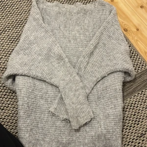 Grå stickad tröja med lång ärm - Mysig grå stickad tröja med lång ärm och avslappnad passform. Perfekt för kyliga dagar och enkel att matcha med jeans eller kjol. Tröjan har en klassisk rund halsringning och är tillverkad i ett mjukt, stickat material.