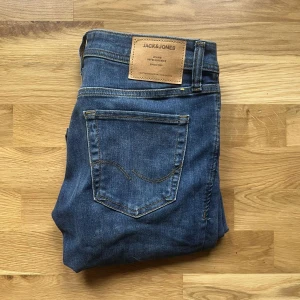 Jack & Jones jeans  - Säljer ett par blå skinny jeans från Jack & Jones, modell Skinny Liam. Klassisk femficksdesign, snygga kontrastsömmar och läderpatch bak i midjan. Jeansen är i stretchigt denim för en tight passform och har en mörkblå tvätt med lätt slitning. Längd 104cm
