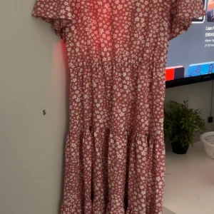 Blommig röd klänning från SHEIN - Supersöt rosa klänning från SHEIN med vita blommor, kort ärm och volangig kjol. Perfekt för sommarens alla tillfällen! Lätt och luftig modell som sitter skönt och har en avslappnad passform.