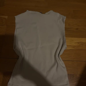 Beige ärmlös topp från Zara - Säljer en stilren beige ärmlös topp från Zara. Toppen har en enkel, rak passform och är tillverkad i mjuk bomull. Perfekt att matcha med jeans eller kjol för en clean look.