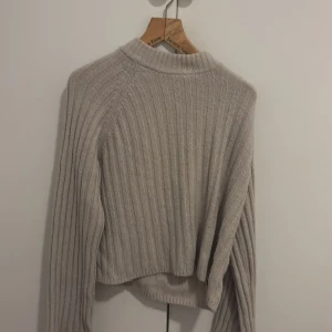 Beige ribbad stickad tröja H&M - Supermjuk beige stickad tröja från H&M i storlek S. Tröjan har ribbat mönster, lång ärm och en lite högre krage. Perfekt för lager-på-lager och chill dagar. Enkel att matcha med jeans eller kjol.