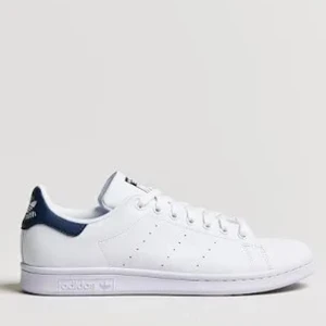 Adidas Stan Smith vita sneakers - Klassiska vita Adidas Stan Smith sneakers med marinblå detalj på hälen. Skorna har rund tå, snörning och är tillverkade i slätt skinn. Perfekta för  sommaren/höst