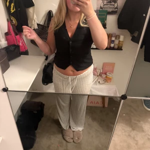 Svart väst från Vero Moda - Snygg svart väst från Vero Moda med klassisk v-ringning och knappar framtill. Västen har en figurnära passform och är perfekt att styla över en t-shirt eller skjorta. Materialet är slätt och ger en stilren look.