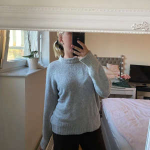 Ljusgrå stickad tröja med rund hals - Mysig ljusgrå stickad tröja med rund halsringning och ribbade muddar. Tröjan har en relaxed passform och långa ärmar, perfekt för kyliga dagar. Enkel och stilren design som funkar till det mesta.