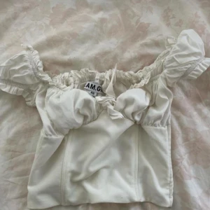 Vit offshoulder topp I.AM.GIA Naomi - Supersöt vit offshoulder topp från I.AM.GIA med puffiga ärmar och knytdetalj framtill. Toppen har en romantisk känsla med rynkade detaljer och sitter snyggt över bysten. Perfekt att styla med jeans eller kjol. 