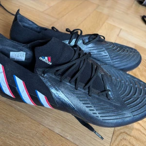 Svarta adidas fotbollsskor  - Snygga svarta adidas fotbollsskor med  3-stripes i vitt, rött och blått på sidan. 