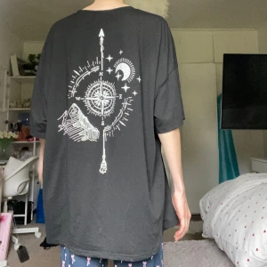 Svart t-shirt - Svart oversized t-shirt med vit grafisk print på ryggen som visar en kompass, berg, måne och stjärnor. T-shirten har rund hals och korta ärmar. Skön och loose passform, perfekt för en chill och avslappnad stil😻Jag använde denna som sovtröja, täcker precis min rumpa. Storlek XL, så passar många, det beror bara vad du vill ha den till och som💕Använd några gånger, inga fel!!💋