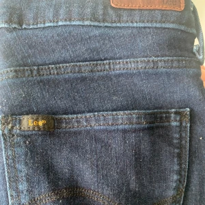 Mörkblå jeans från Lee - Snygga mörkblå jeans från Lee med klassisk femficksdesign och läderpatch bak i midjan. Jeansen har raka ben och är tillverkade i robust denim med tydliga sömmar. Perfekta för dig som gillar en tidlös och clean look.